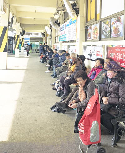 지난 10일 고현시내버스터미널에서 버스를 기다리고 있는 시민들 뒤로 '시내버스 노선 조정안내' 현수막이 게재돼 있다.